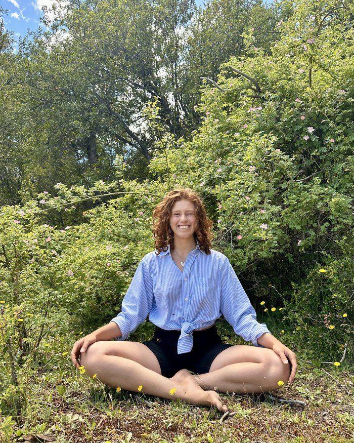 Jazmin sitting cross-legged in a sunlit meadow